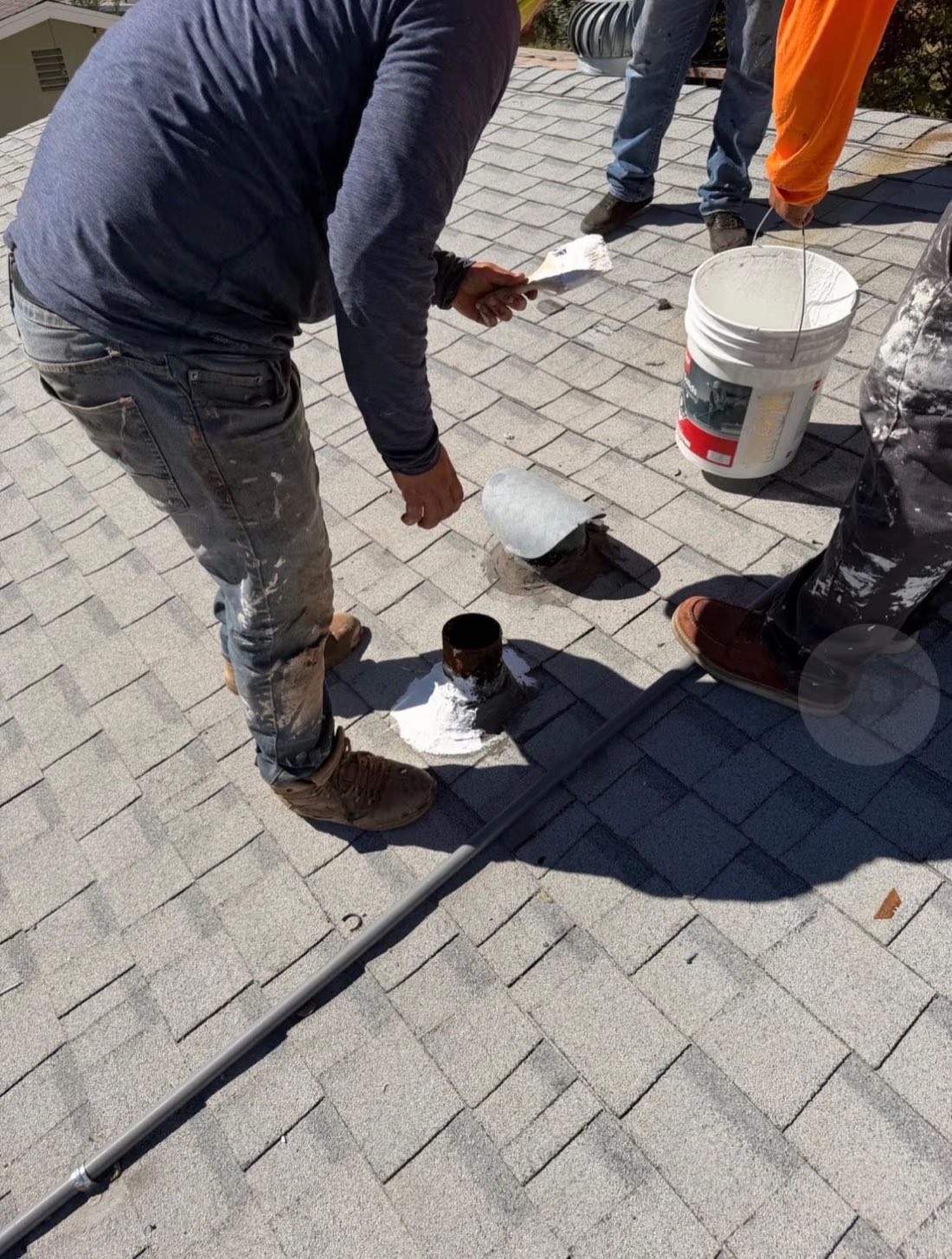 Integrity Roofing crew coating roof vents on a shingle roof